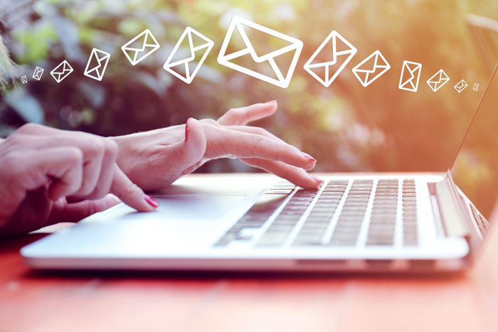 Hands typing on a laptop outdoors with envelope symbols above laptop. Email campaigns are part of corporate event planning tips. 